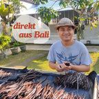 Vanilleproduzent auf Bali mit einem Strohhut, umgeben von geernteten und getrockneten Vanilleschoten.